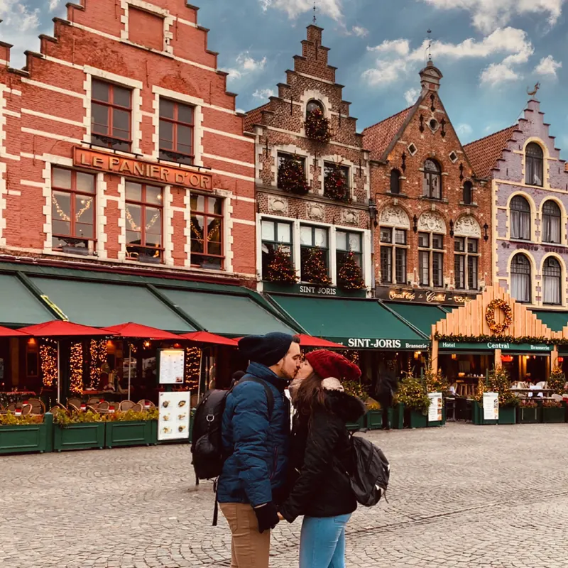 Inma y Álex besándose en el Grote Markt de Brujas, con las casas gremiales decoradas por Navidad