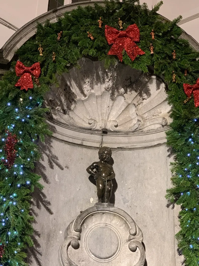 El Manneken Pis de Bruselas con su decoración navideña de guirnaldas y lazos rojos