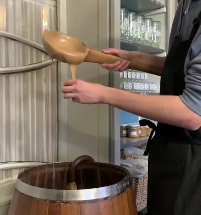 Dependiente de Tierenteyn-Verlent sacando mostaza de Gante de un barril con un cucharón de madera
