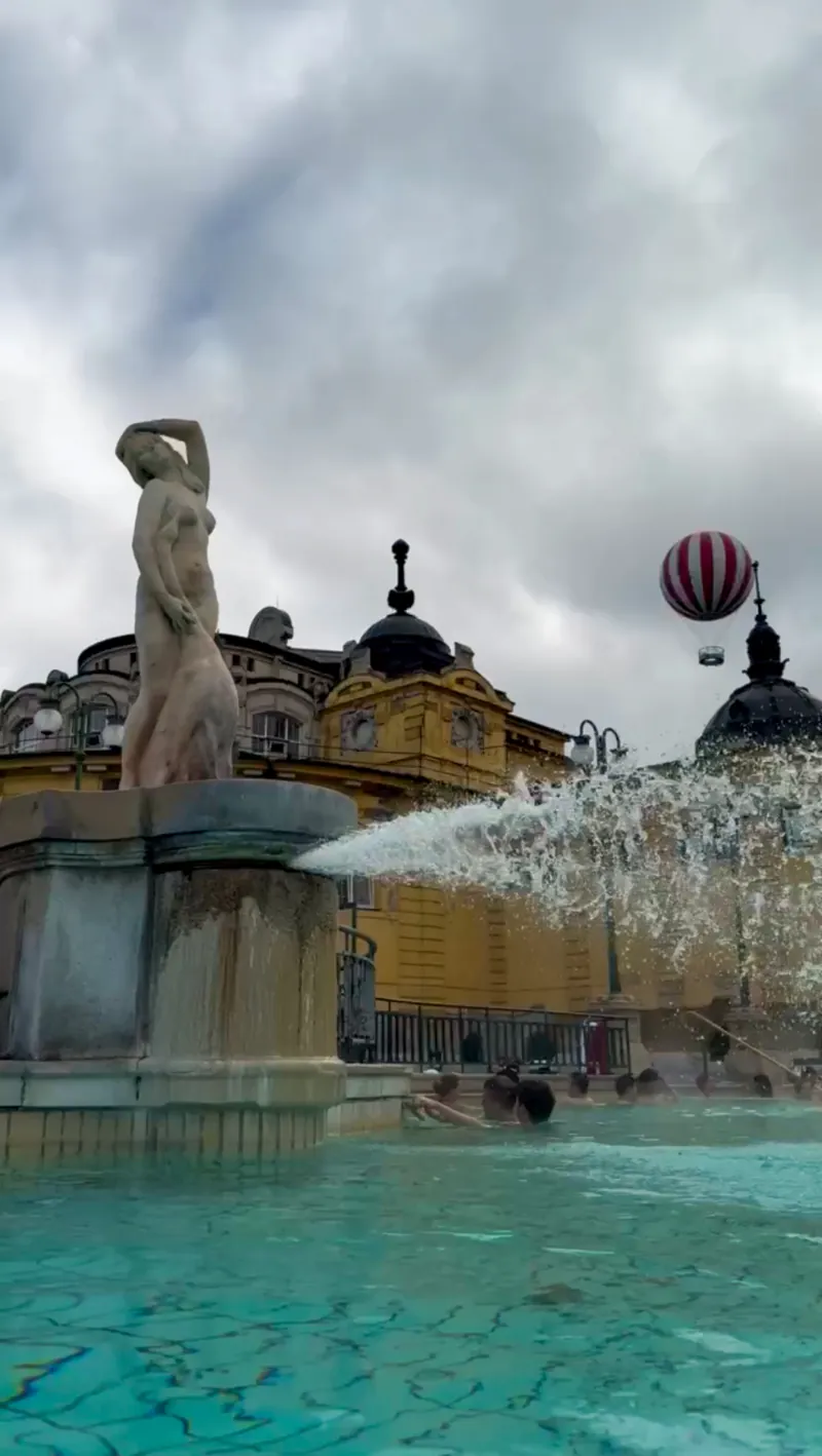 Fuente de la piscina exterior de los baños Széchenyi, con el edificio amarillo y un globo aerostático al fondo