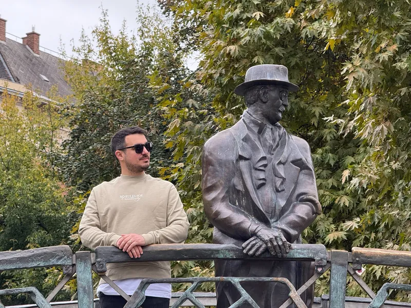 Álex junto a la estatua de bronce de Imre Nagy, apoyada en la barandilla de un pequeño puente, en Budapest