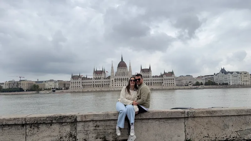 Inma y Álex sentados en el muro de la orilla de Buda, con el Parlamento de Budapest y el Danubio al fondo