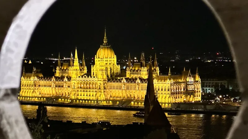 El Parlamento de Budapest iluminado de noche sobre el Danubio, visto a través de un hueco del muro del Bastión de los Pescadores