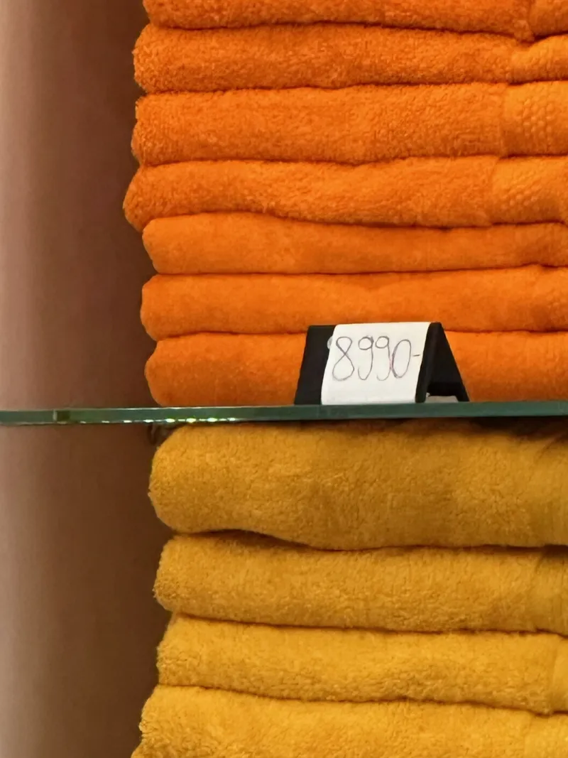 Toallas naranjas y amarillas a la venta en los baños Széchenyi de Budapest, con un cartel escrito a mano de 8.990 florines