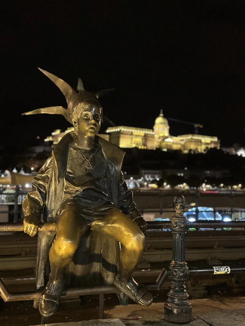Estatua de la Princesita en el paseo del Danubio, con el castillo de Buda iluminado de noche